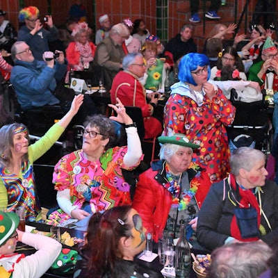 Bunt verkleidete Menschen sitzen im Publikum und winken mit den Armen.
