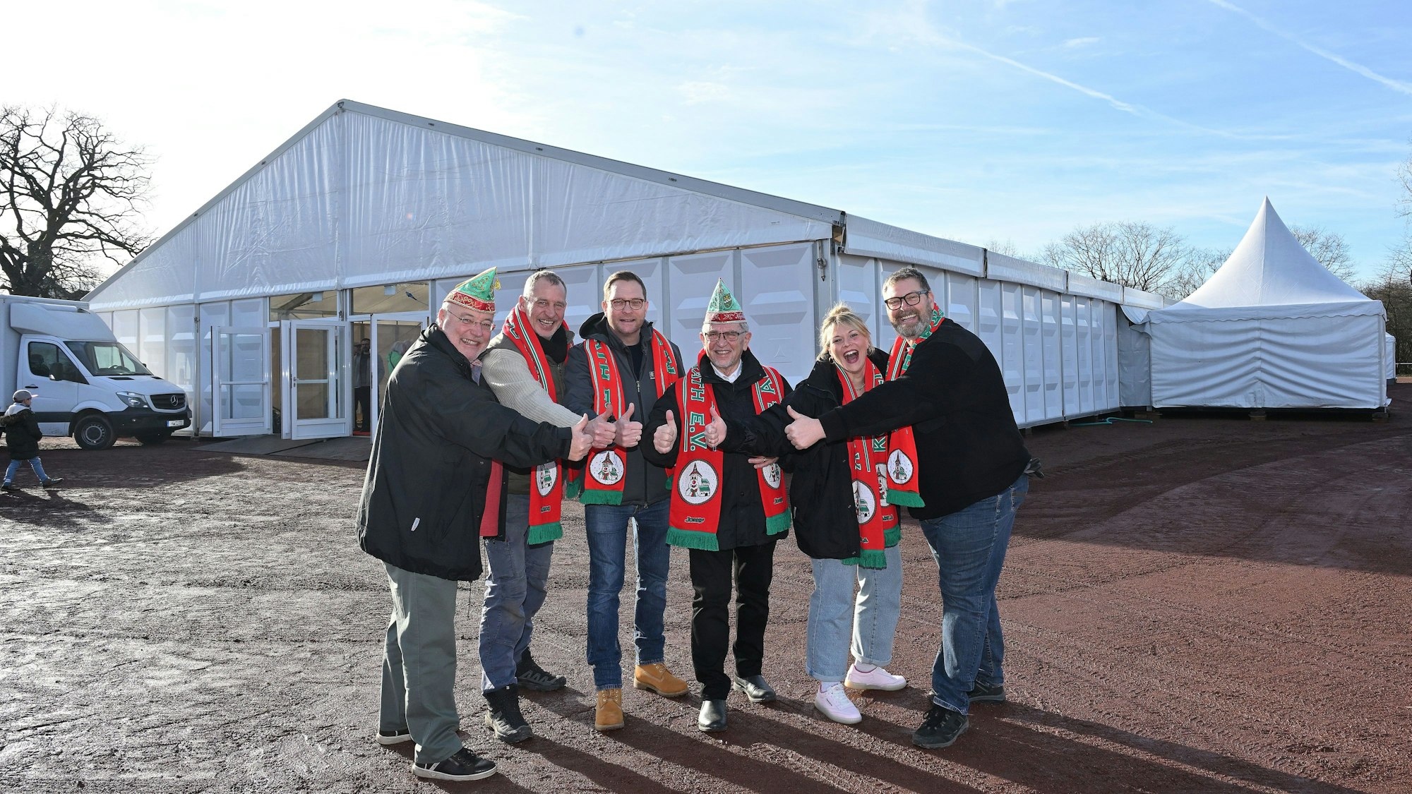 Sechs Menschen im Halbkreis, alle tragen einen Schal des Karnevalsvereins, einige ein Narrenkappe. Im Hintergrund das Festzelt.