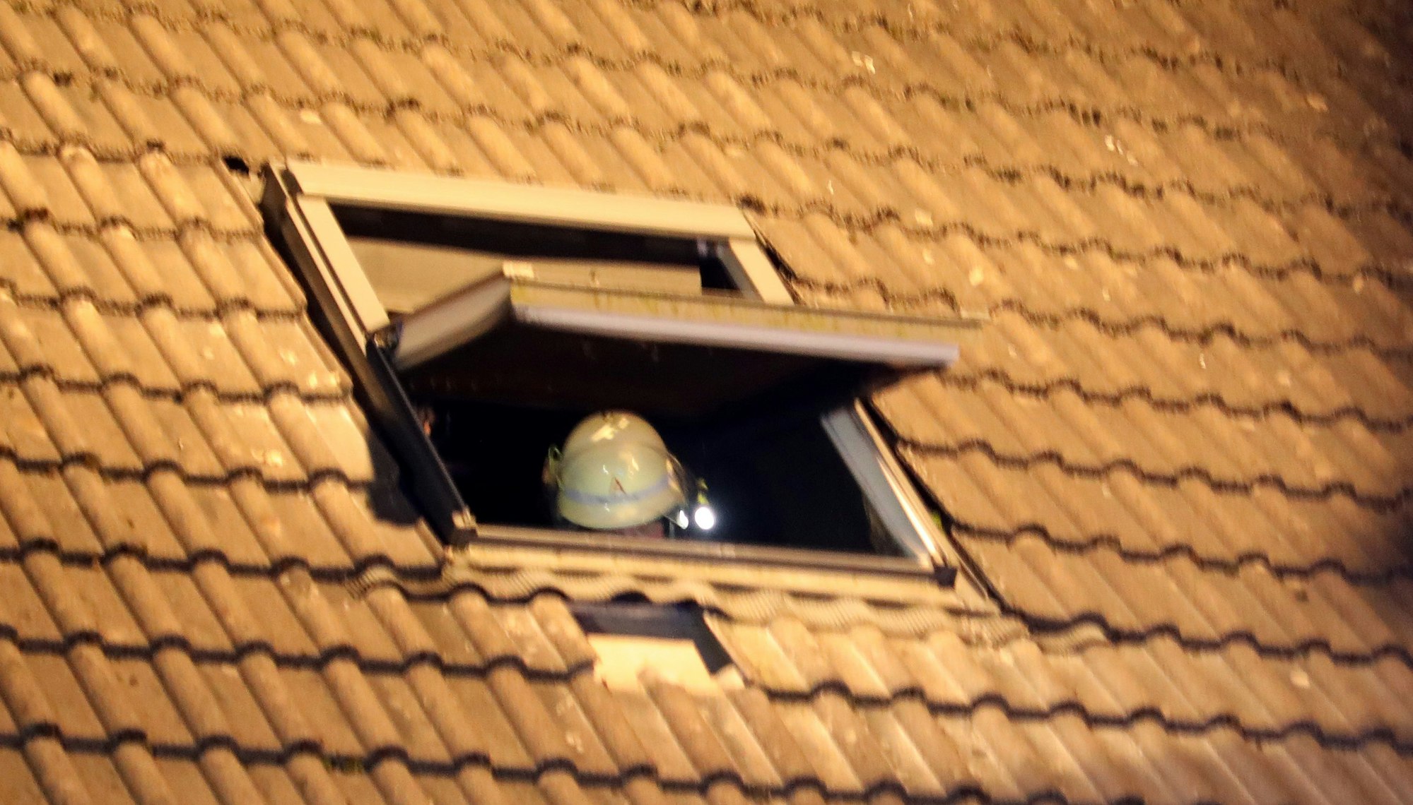 In einem Dachfenster ist der Helm eines Feuerwehrmanns zu sehen.