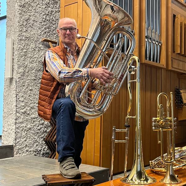 Ein Mann steht mit einer Tuba im Arm vor einer Orgel, vor ihm stehen weitere Blasinstrumente.