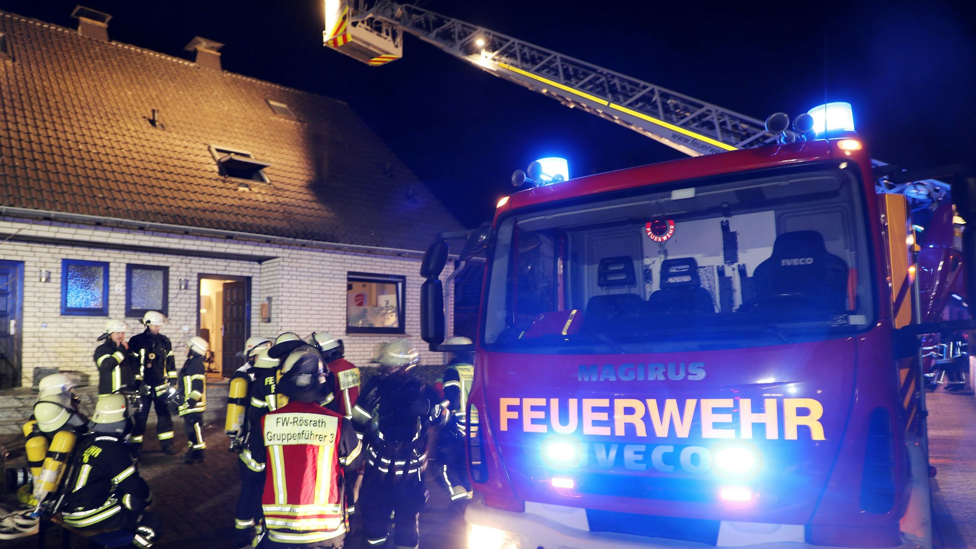 Eine Drehleiter steht vor einem Wohnhaus in der Straße Wiedenhof in Rösrath-Forsbach. Feuerwehrleute sind im Einsatz auf der Straße und am Haus.
