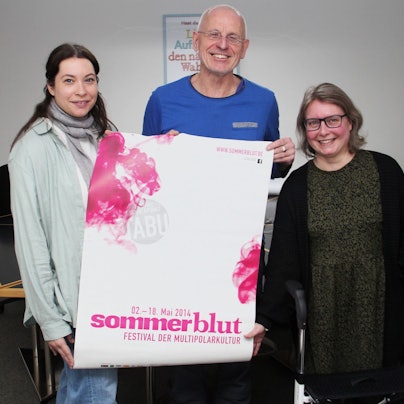 Zwei Frauen und ein Mann stehen nebeneinander. Der Mann hält ein Plakat, auf dem „Sommerblut“ zu lesen ist.