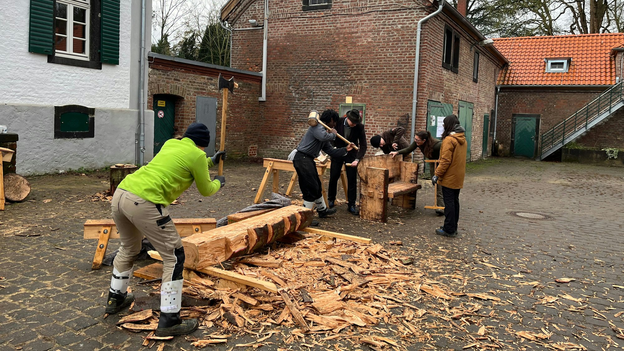 Im Innenhof eines Gutshofs arbeiten junge Leute an einem Baumstamm.