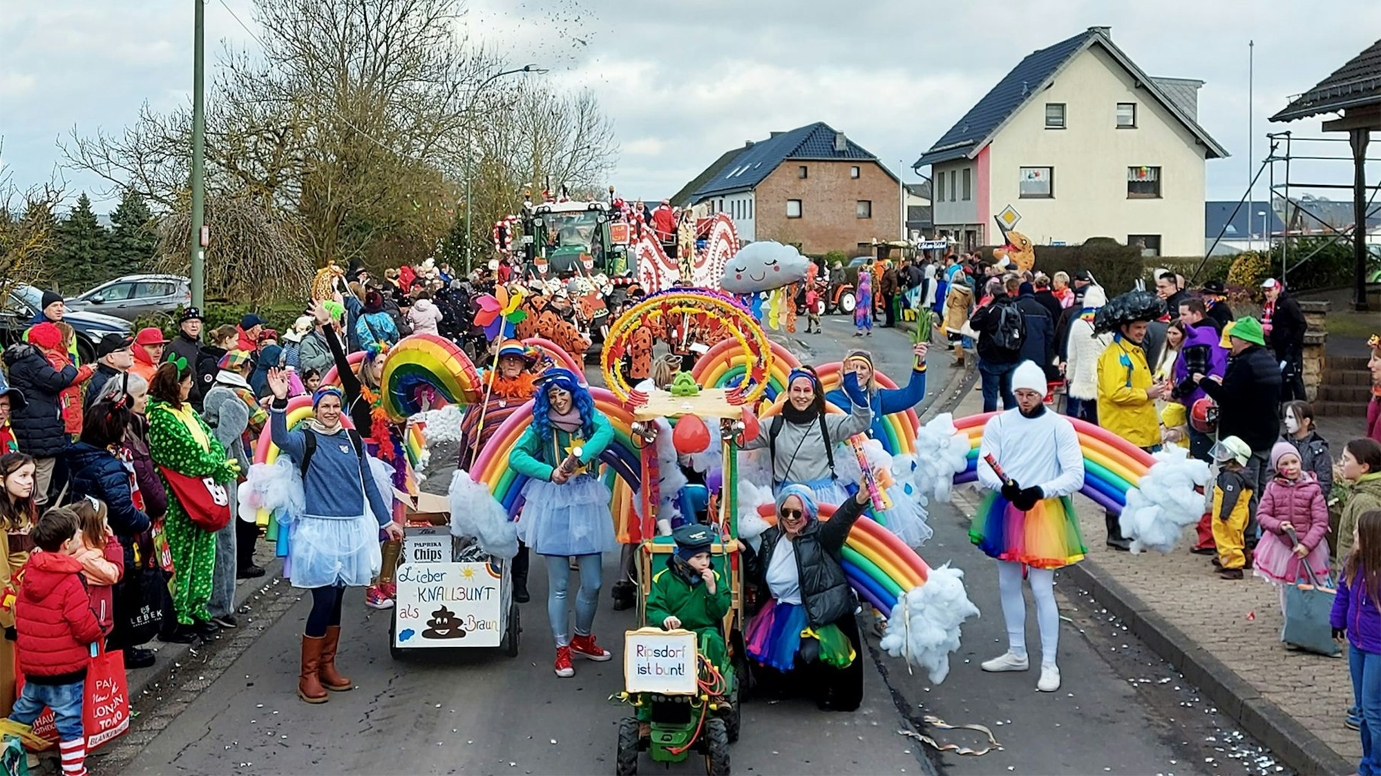 Eine als Regenbögen und Wolken kostümierte Gruppe läuft im Ripsdorfer Zug mit und jubelt den Jecken am Straßenrand zu.
