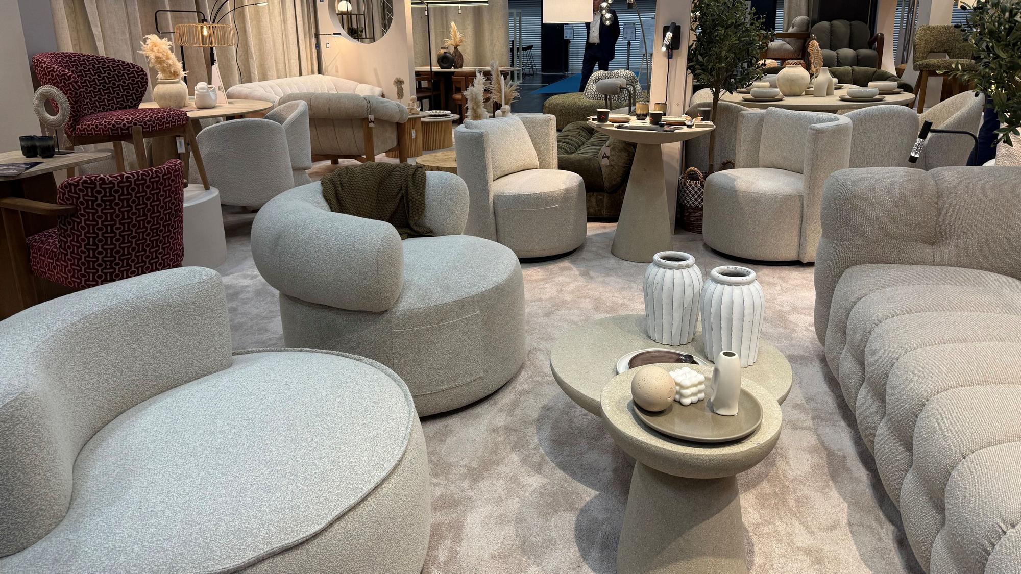 Helle Sofa mit passenden Hockern stehen in einem Ausstellungsraum.