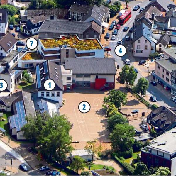 Eine Ansicht der von der Sonne beschienenen Ortsmitte von Hoffnungsthal aus der Vogelperspektive mit Schule, Schulhof, Freibad-Parkplatz und Hauptstraße.