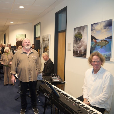 Viele Gäste stehen in einem Korridor das Mechernicher Rathauses. An den Wänden hängen Bilder. Im Vordergrund sitzt ein Mann an einem elektronischen Piano.