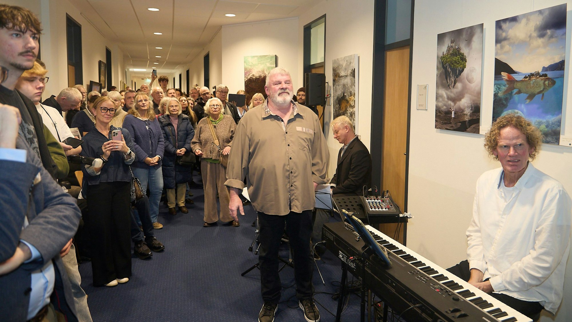 Viele Gäste stehen in einem Korridor das Mechernicher Rathauses. An den Wänden hängen Bilder. Im Vordergrund sitzt ein Mann an einem elektronischen Piano.