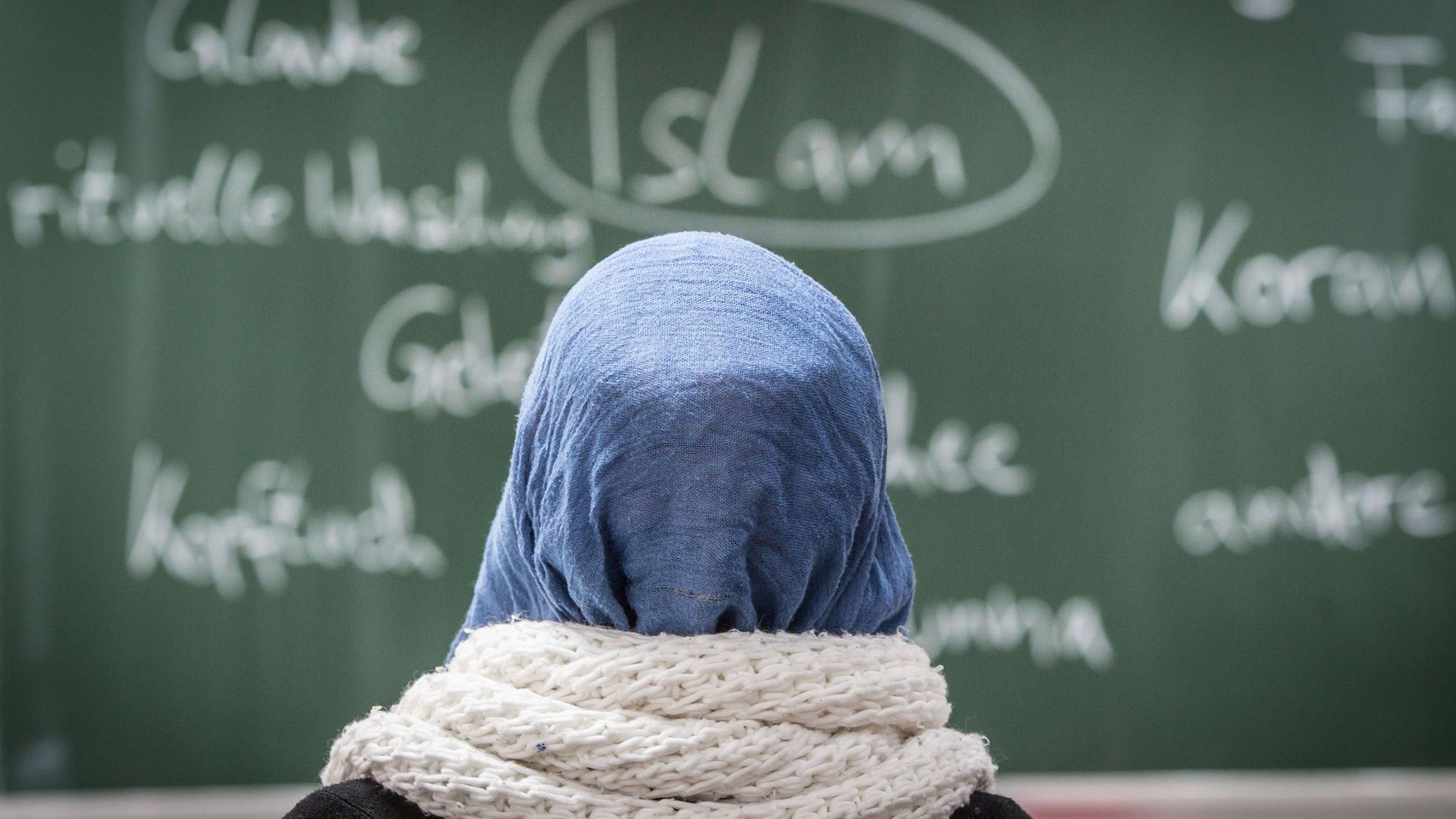 Eine Schülerin mit Kopftuch sitzt bei einer Unterrichtsstunde zum Thema Islam vor einer Tafel.