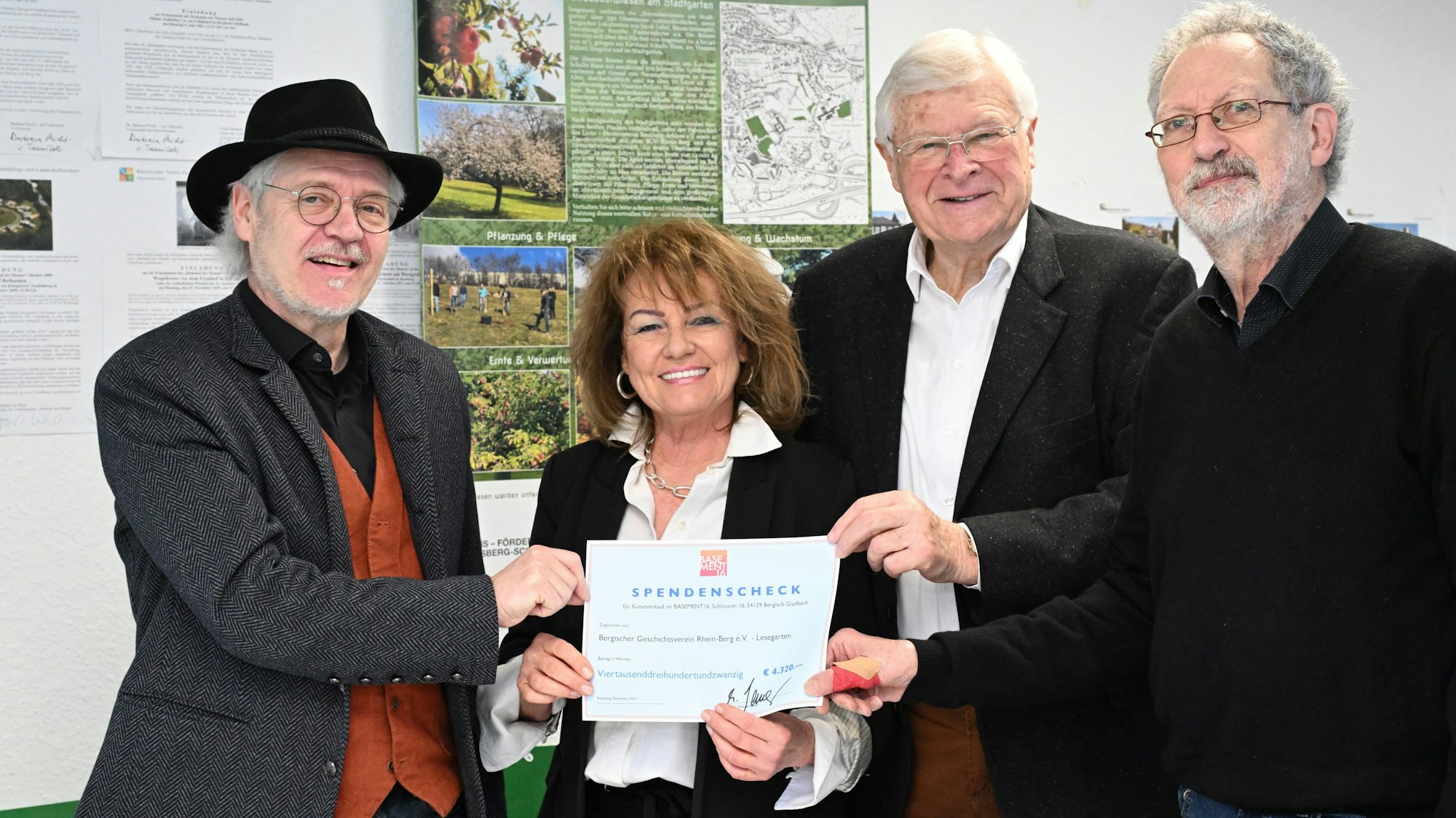 Drei Männer und eine Frau präsentieren lachend einen Spendenscheck