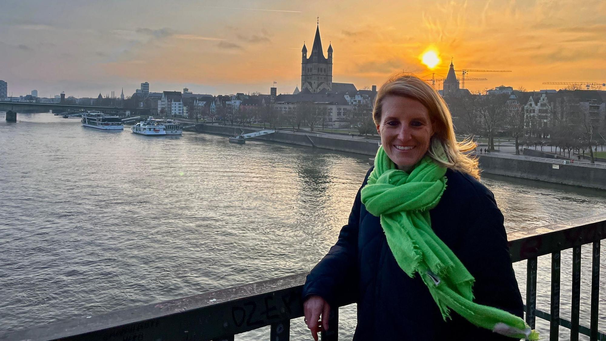 Eine Frau mit grünem Schal steht vor einem großen Schiff.