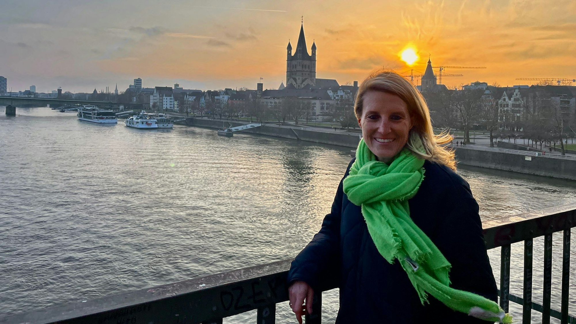 Eine Frau mit grünem Schal steht vor einem großen Schiff.