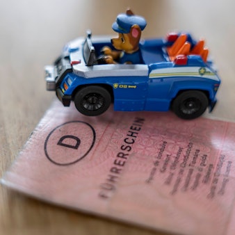 Das Bild zeigt einen Papierführerschein, der nun getauscht werden muss und ein Spielzeugauto, in dem eine Hundefigur sitzt.