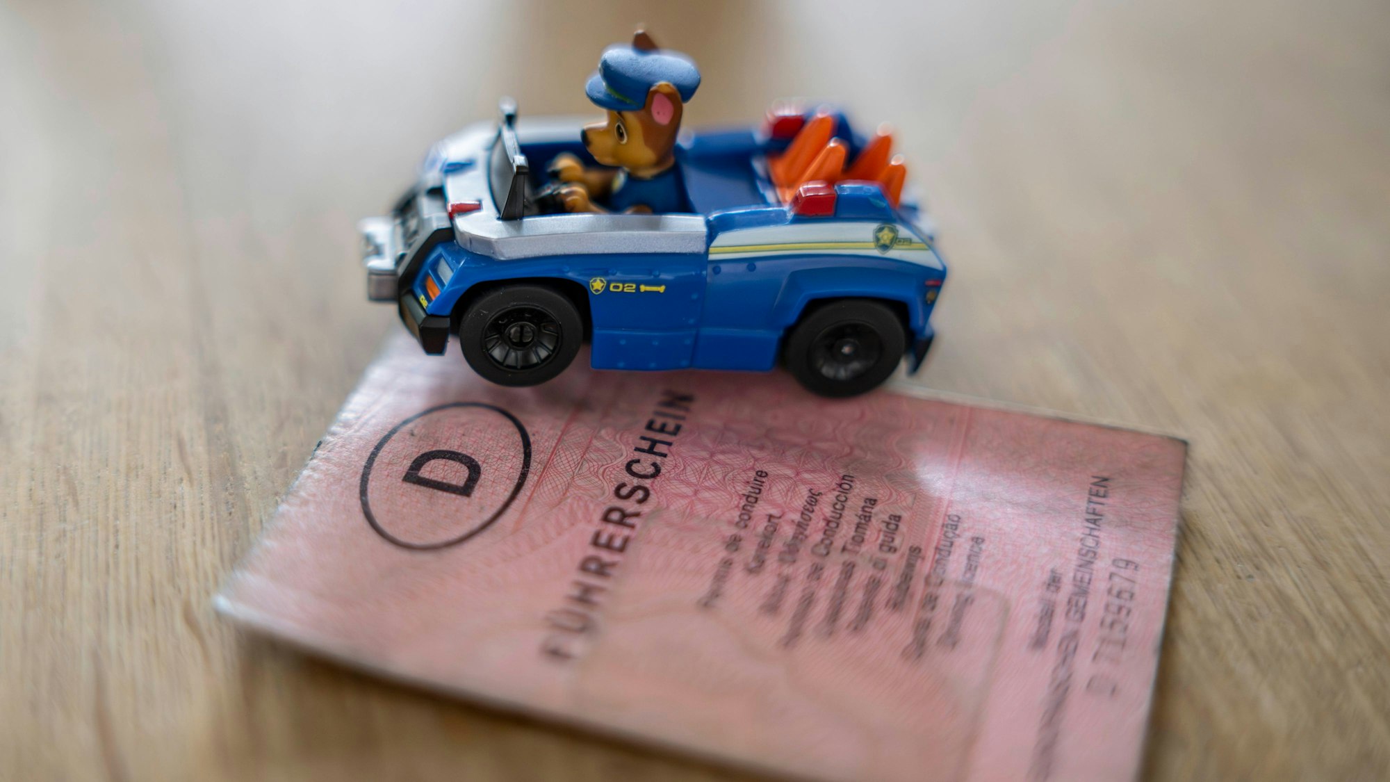 Das Bild zeigt einen Papierführerschein, der nun getauscht werden muss und ein Spielzeugauto, in dem eine Hundefigur sitzt.