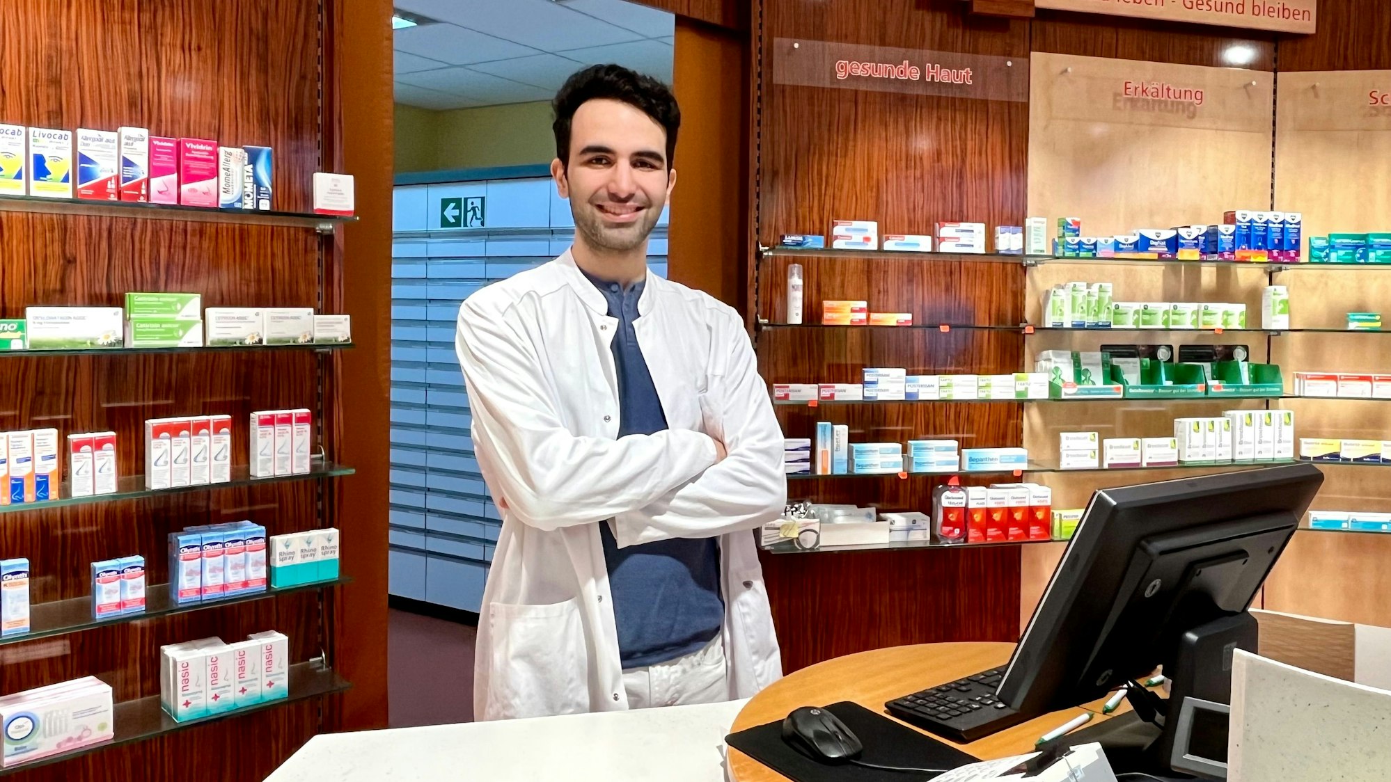 Ein Mann in weißem Kittel steht in einer Apotheke.