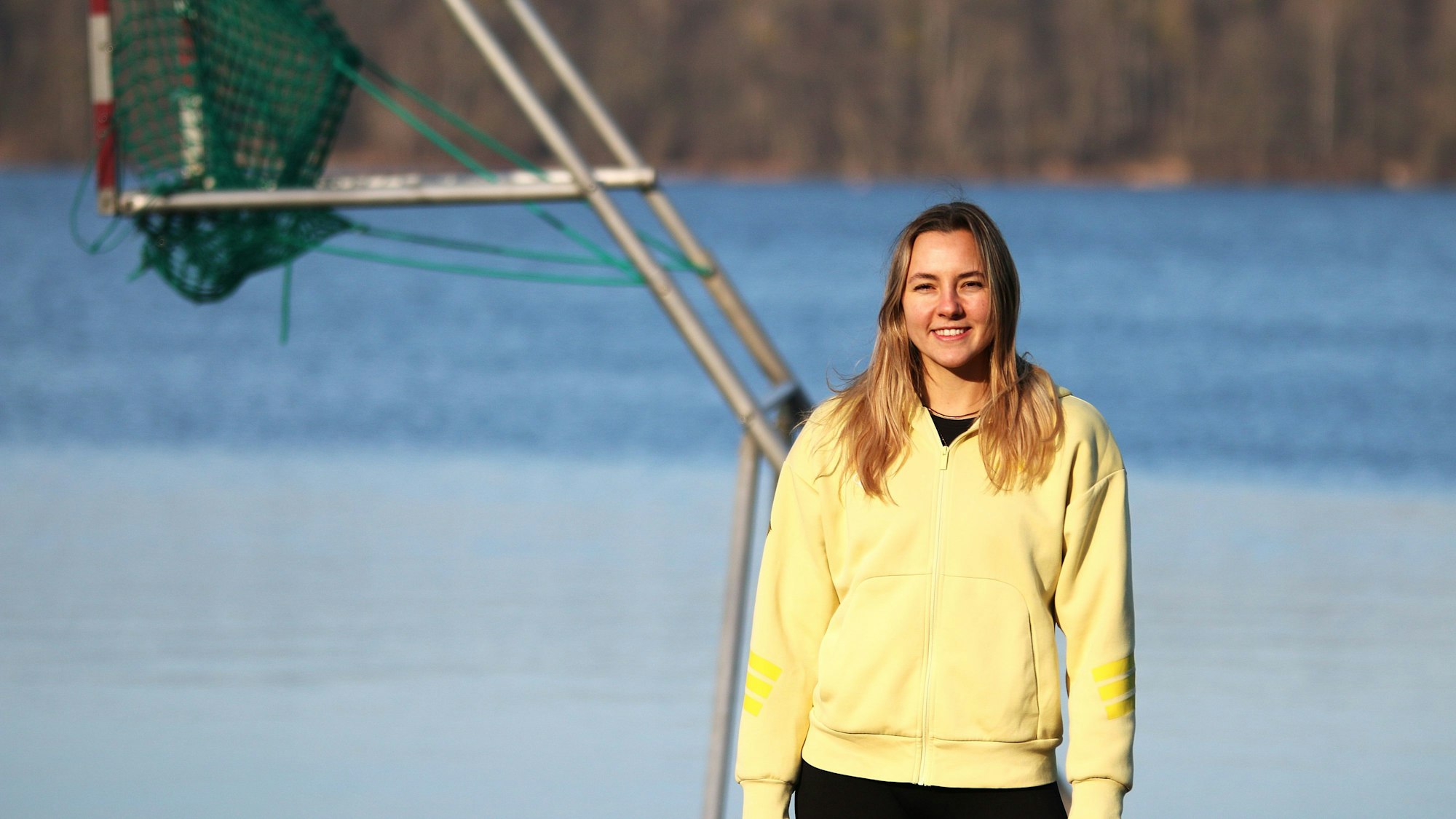 Portrait von Leonie Wagner in gelber Team-D-Jacke, im Hintergrund ist das Netz des Kanupolotors zu sehen