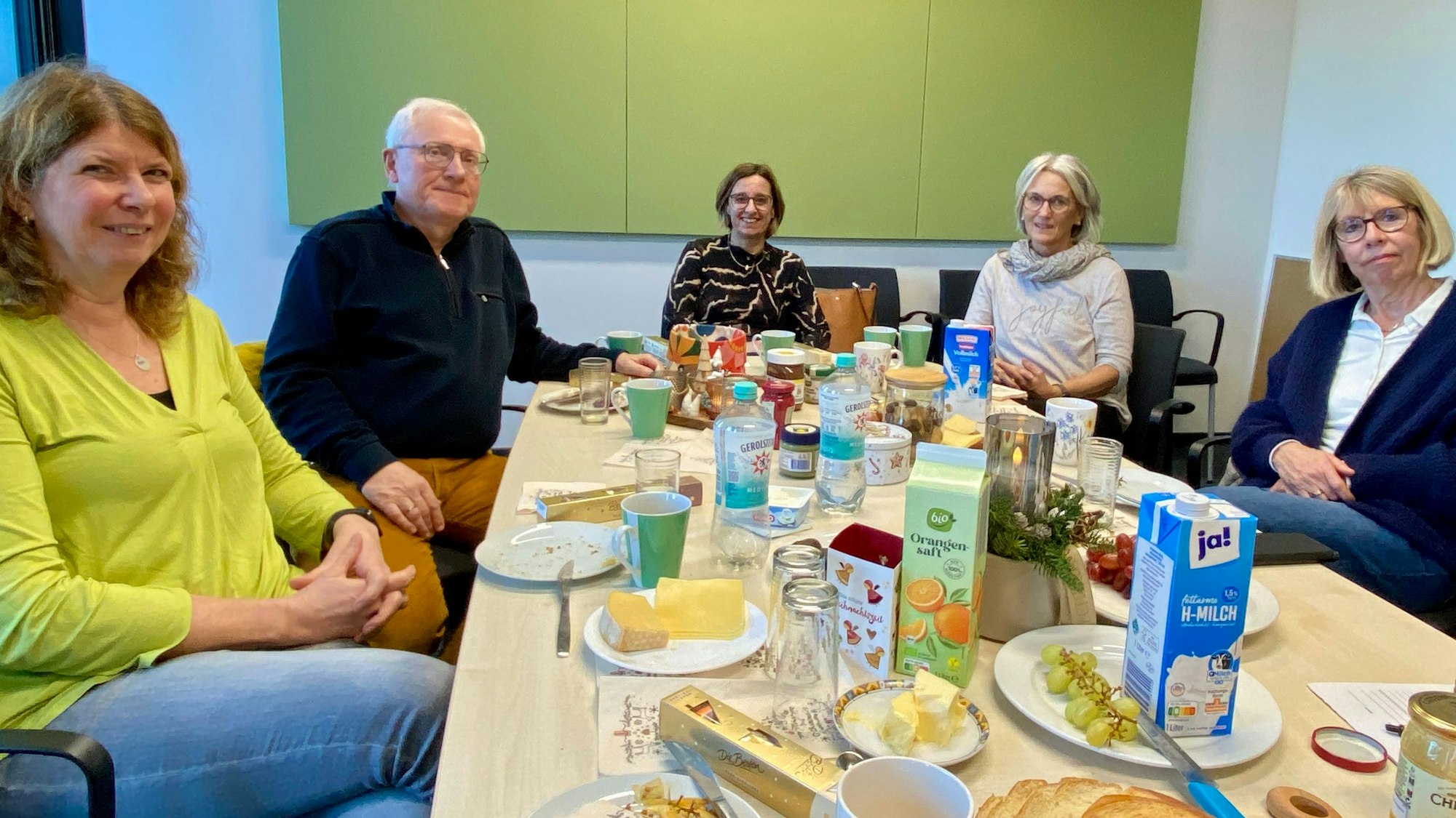 Vier Frauen und ein Mann sitzen an einem langen Frühstückstisch, auf dem Speisen und Getränke angerichtet sind.