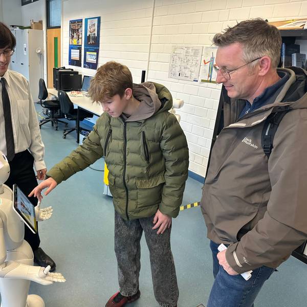 Der 14-jährige Laron Fuchs (M.) ist mit seinem Vater Andreas (r.) aus Windeck gekommen, um sich über Studienmöglichkeiten zu informieren. Jordan Schneider (l.), wissenschaftlicher Mitarbeiter der Hochschule, erklärt ihm die Funktionsweise eines sozialen Roboters.