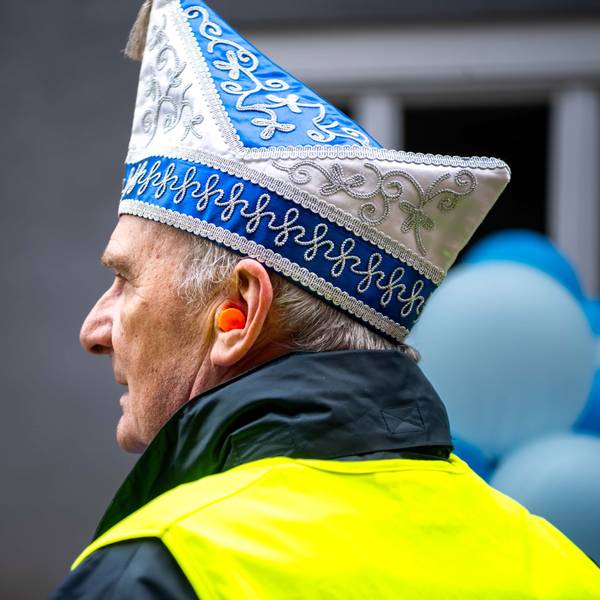 Ein Wagenengel mit Narrenkappe und gelber Warnweste trägt beim Karnevalszug einen Gehörschutz.