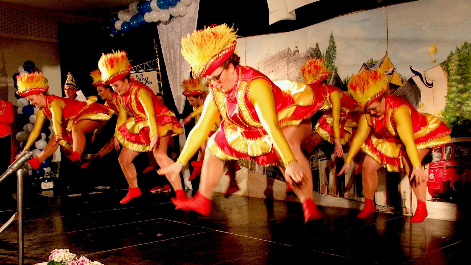 Garde-Tänzerinnen in rot-goldenen Uniformen springen beim Tanz auf der Bühne in die Höhe.