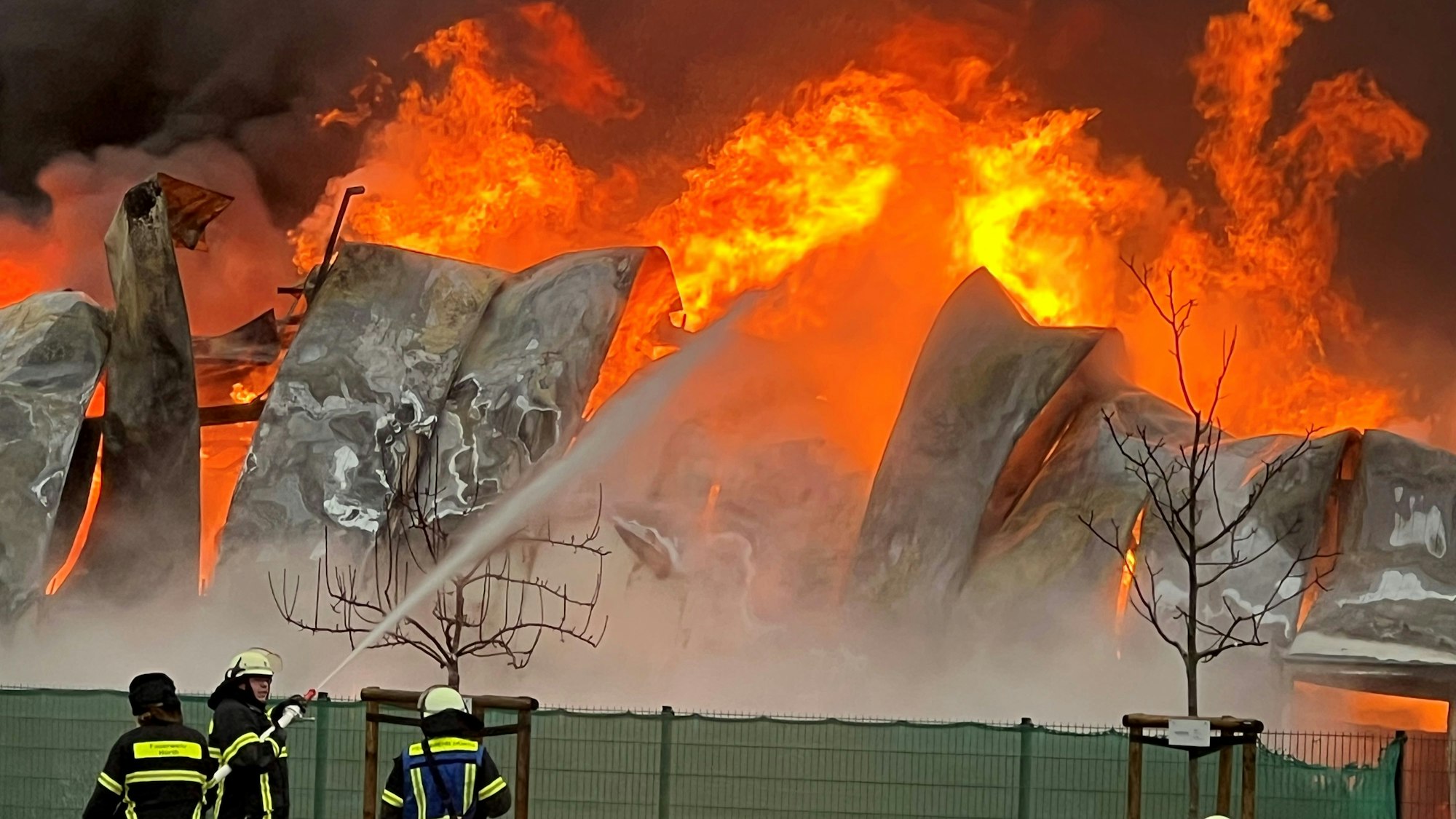 Das Bild zeigt mehrere Feuerwehrleute vor einer brennenden Lagerhalle.