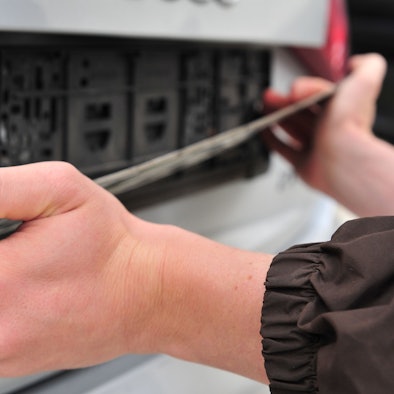 Das Foto zeigt zwei Hände, die nach einem Auto in einem Kennzeichenhalter greifen.