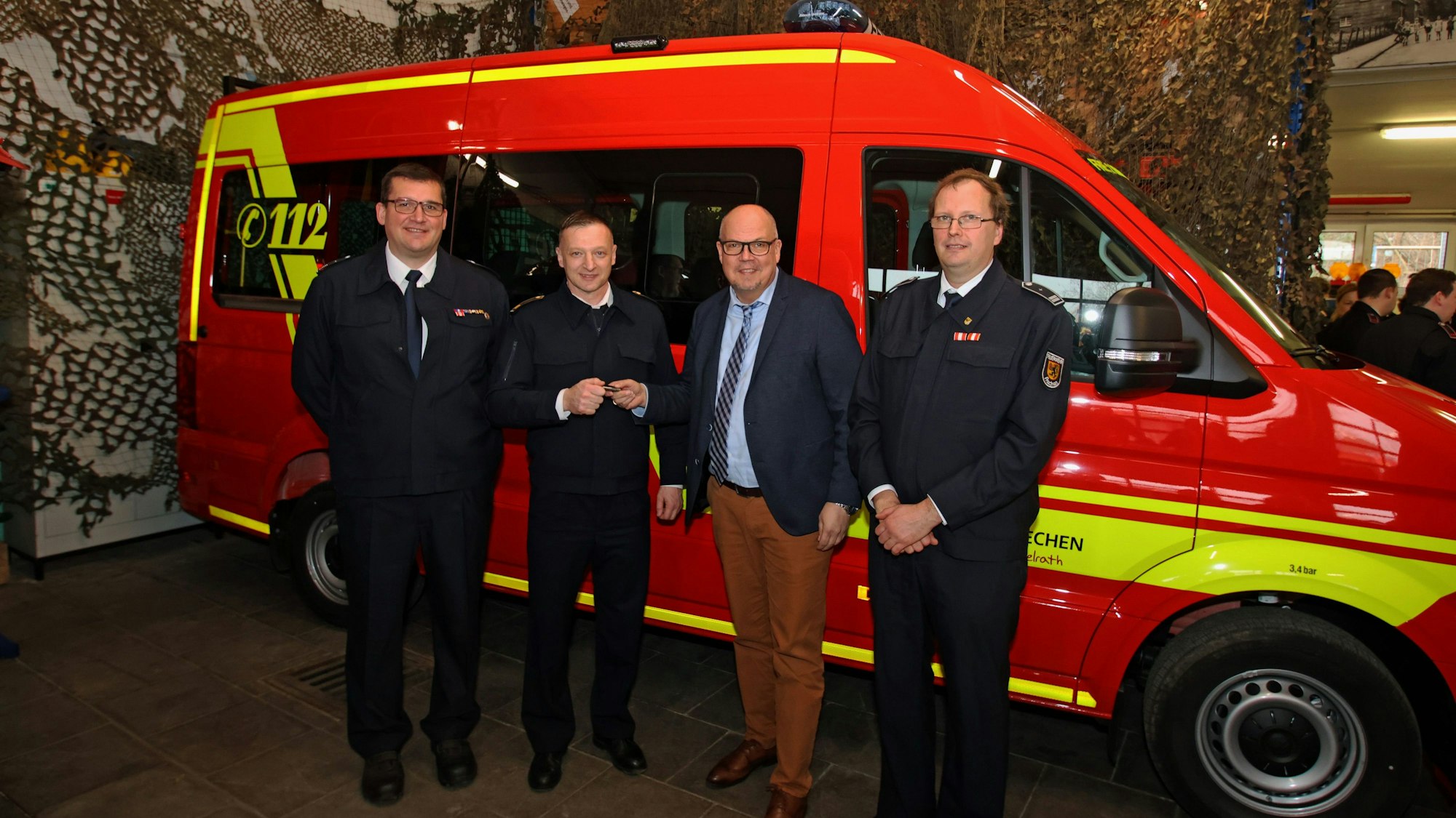 Auf dem Bild sind vier Männer und ein Feuerwehrfahrzeug zu sehen.