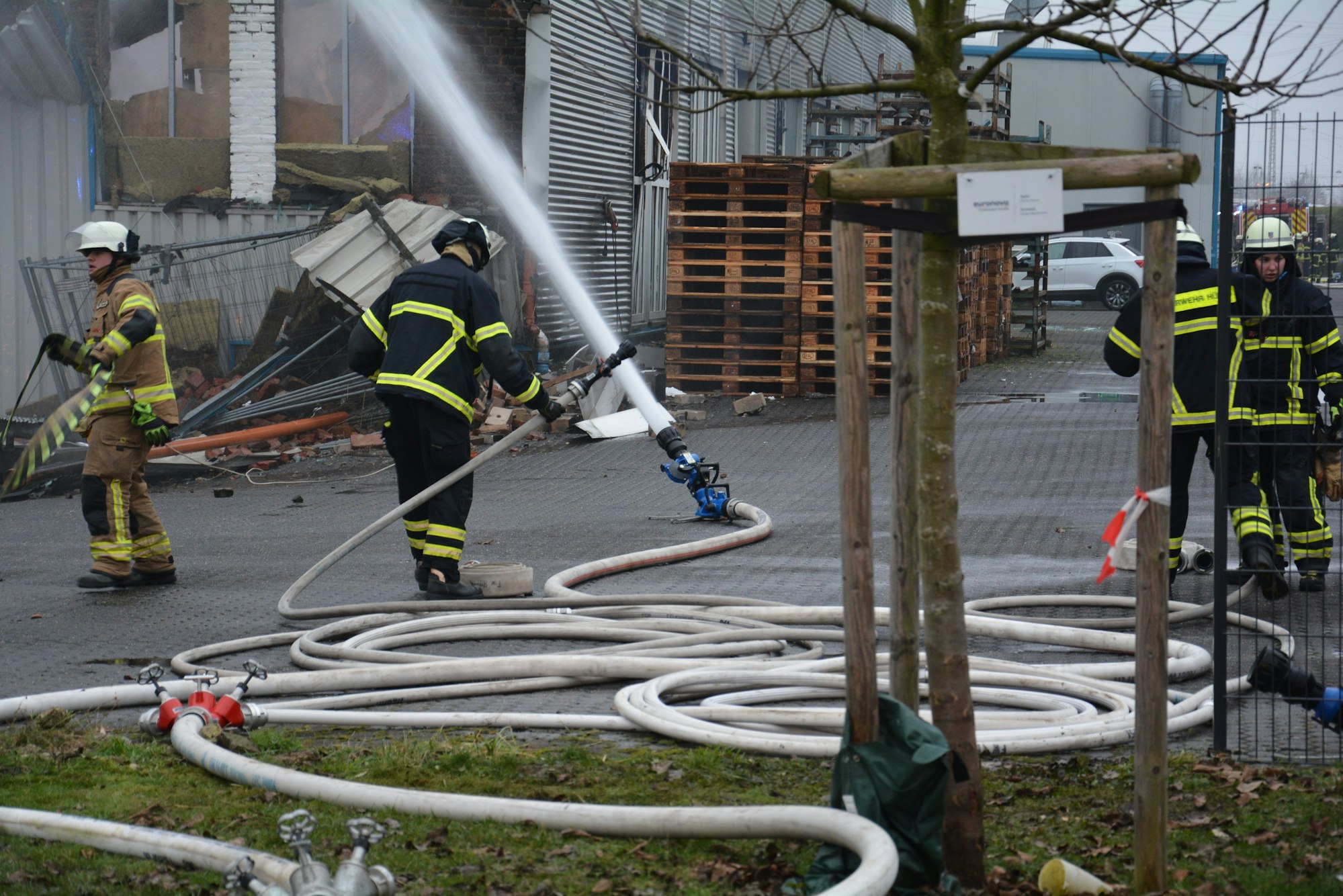 Das Bild zeigt mehrere Feuerwehrleute an der Rückseite einer Lagerhalle.