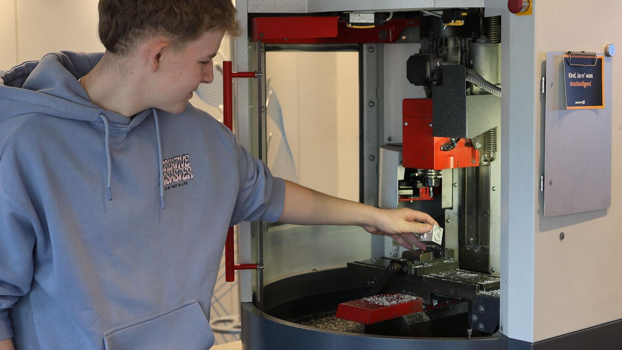 Ein Schüler steht an einer CNC-Fräsmaschine und setzt sie in Gang.