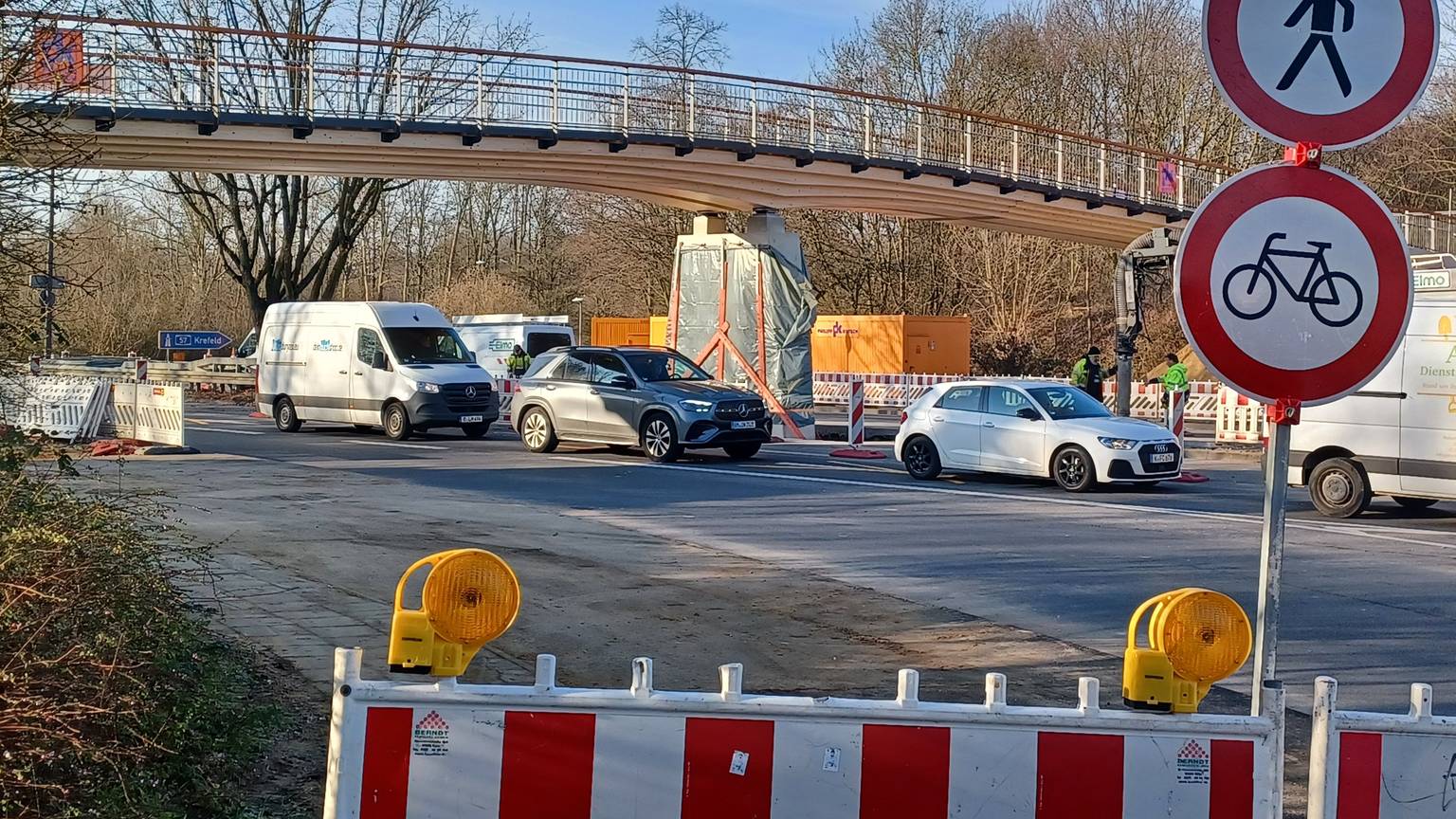Eine nagelneue Rad- und Fußgängerbrücke aus Holz spannt sich über eine mehrspurige Straße.