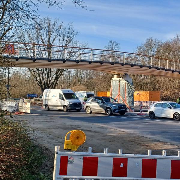 Eine nagelneue Rad- und Fußgängerbrücke aus Holz spannt sich über eine mehrspurige Straße.