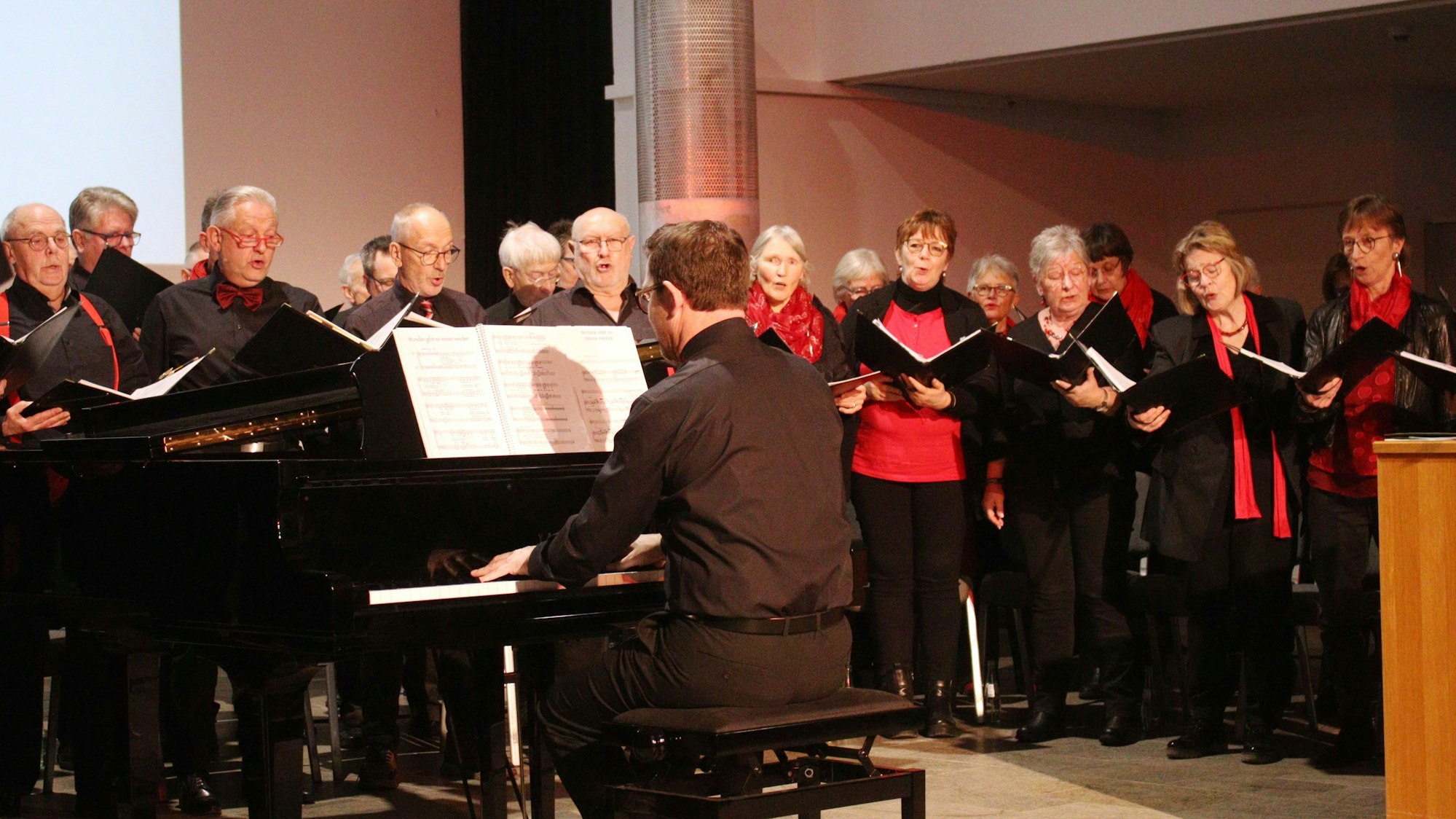 Der Chor des Musikvereins Eifelklang Mutscheid singt beim Neujahrsempfang, begleitet von einem Mann am Klavier.