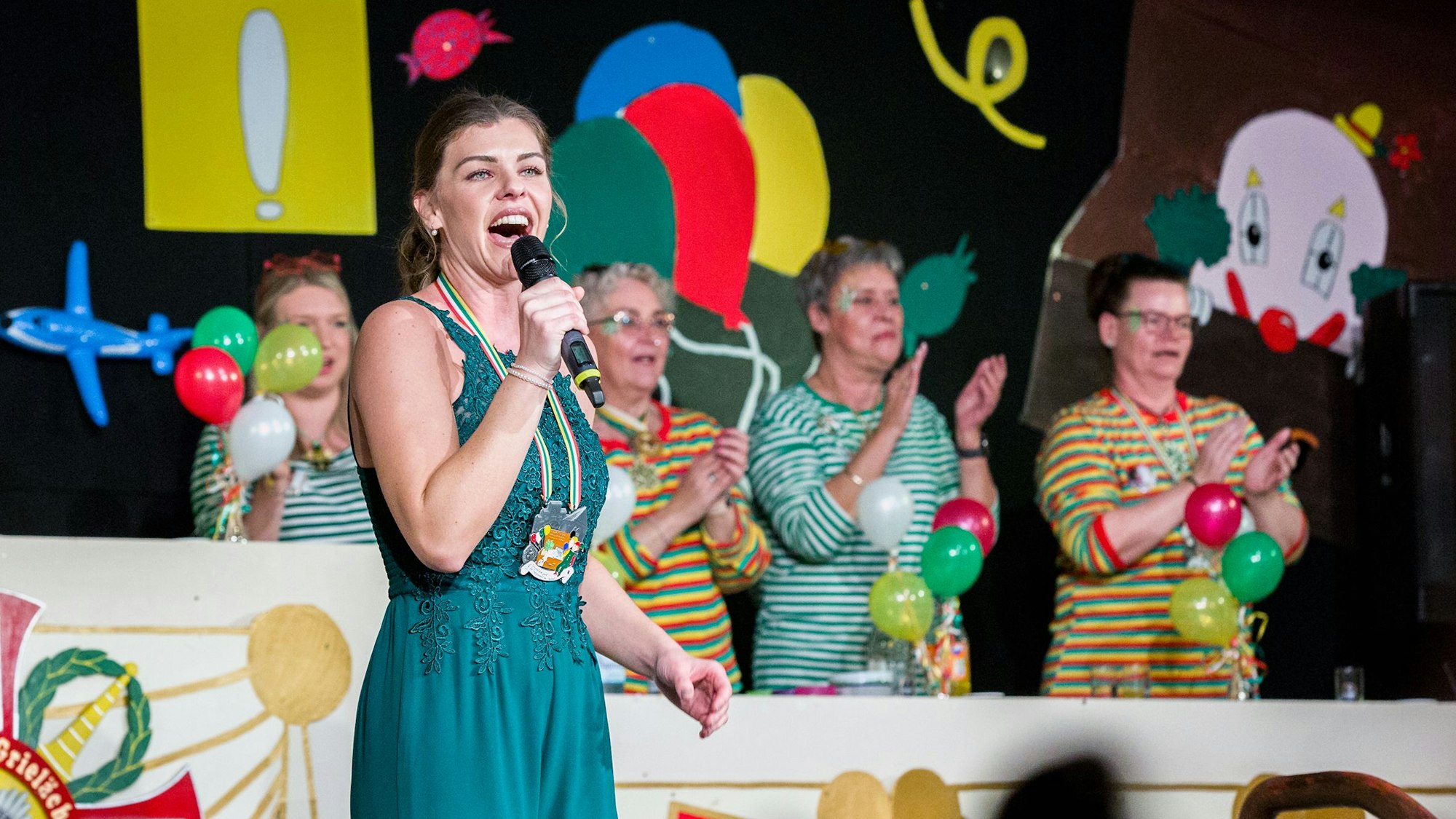 Eine Frau im blauen Kleid steht singend mit Mikrofon in der Hand auf einer Bühne.