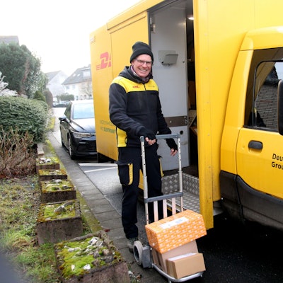 Ein Mann in DHL-Outfit mit einer Sackkarre.