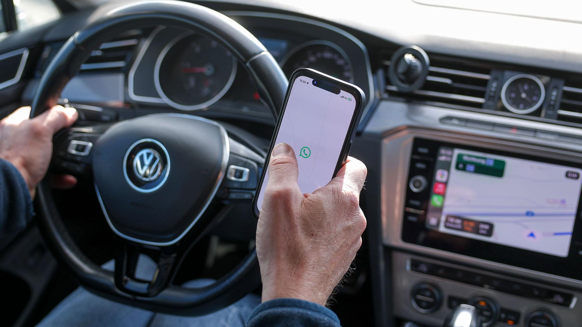 Ein Mann startet den WhatsApp Messenger auf einem Smartphone im Auto.