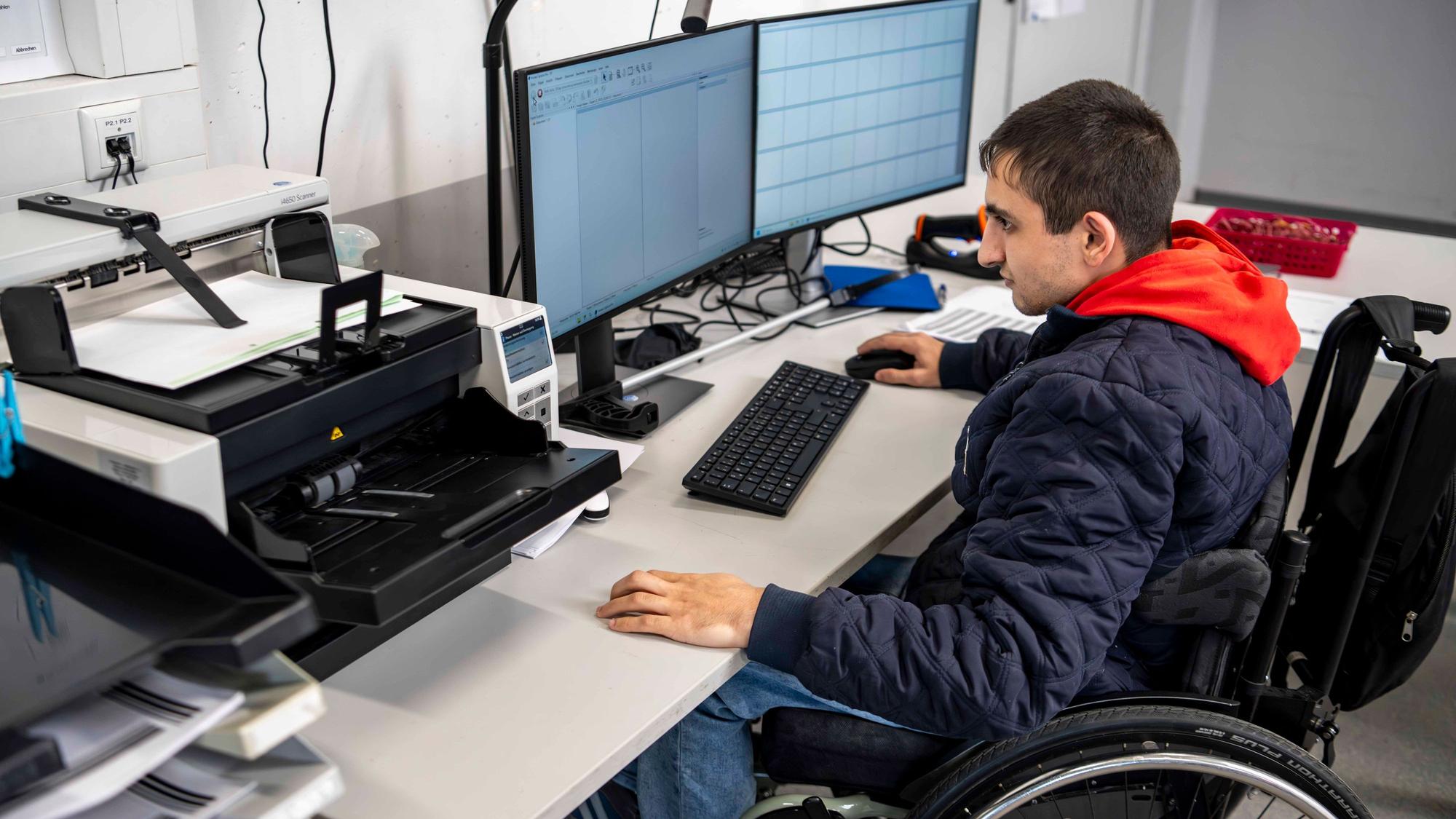 Das Bild zeigt einen Mitarbeiter der NEW, der vor einem Computer sitzt und Akten scannt.