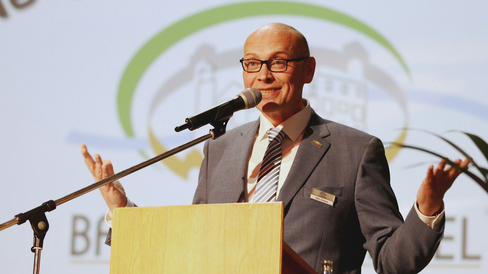 Bad Münstereifels Bürgermeister Sebastian Glatzel steht mit leicht ausgebreiteten Armen an einem Pult und spricht in ein Mikrofon.