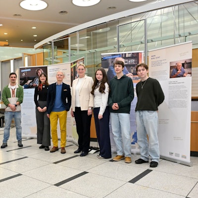 Eine Reihe von zehn Menschen steht im Eingangsbereich der Kreissparkasse Bergisch Gladbach vor Roll-ups, auf denen Texte und Fotos zu sehen sind.