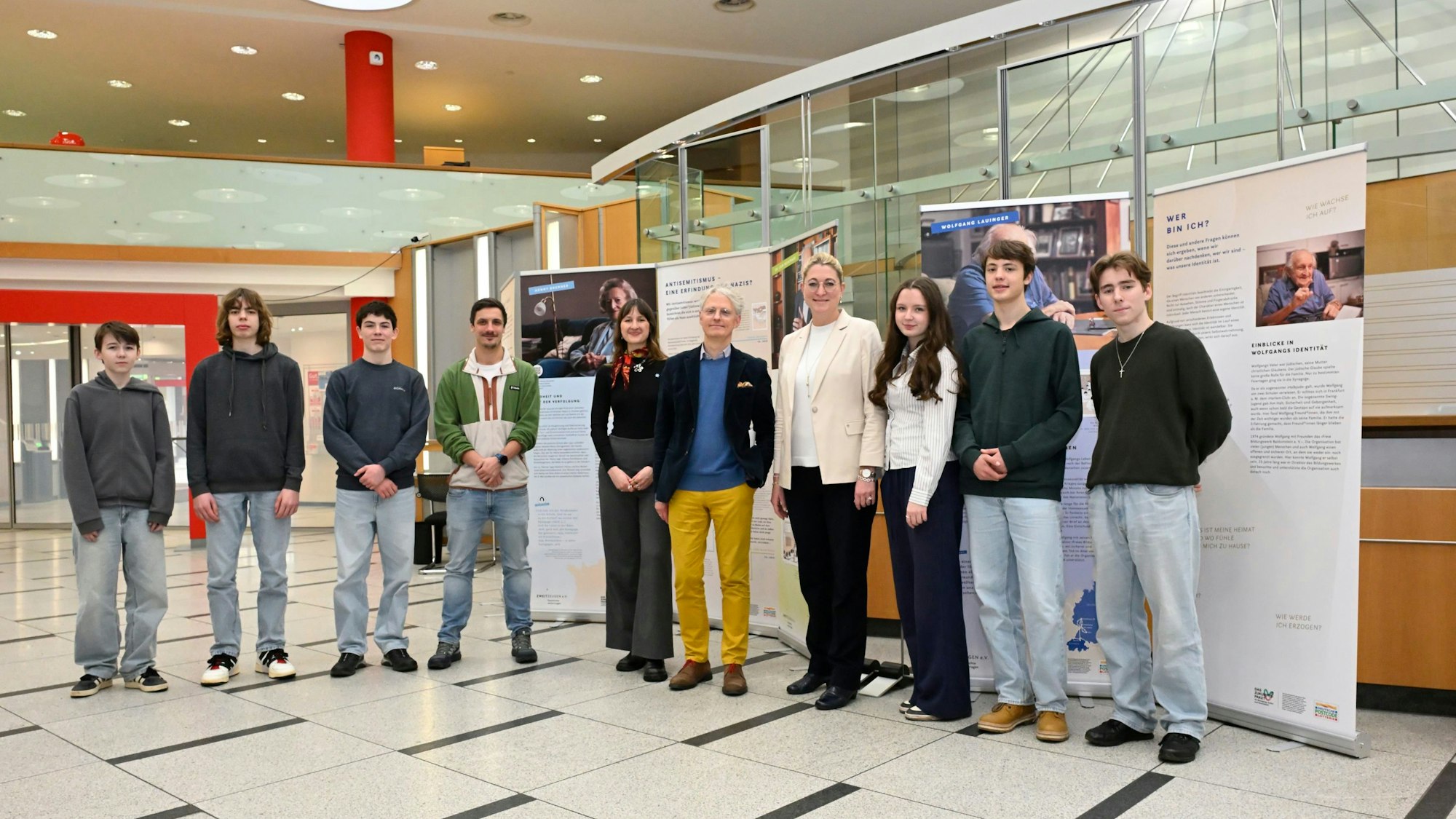 Eine Reihe von zehn Menschen steht im Eingangsbereich der Kreissparkasse Bergisch Gladbach vor Roll-ups, auf denen Texte und Fotos zu sehen sind.