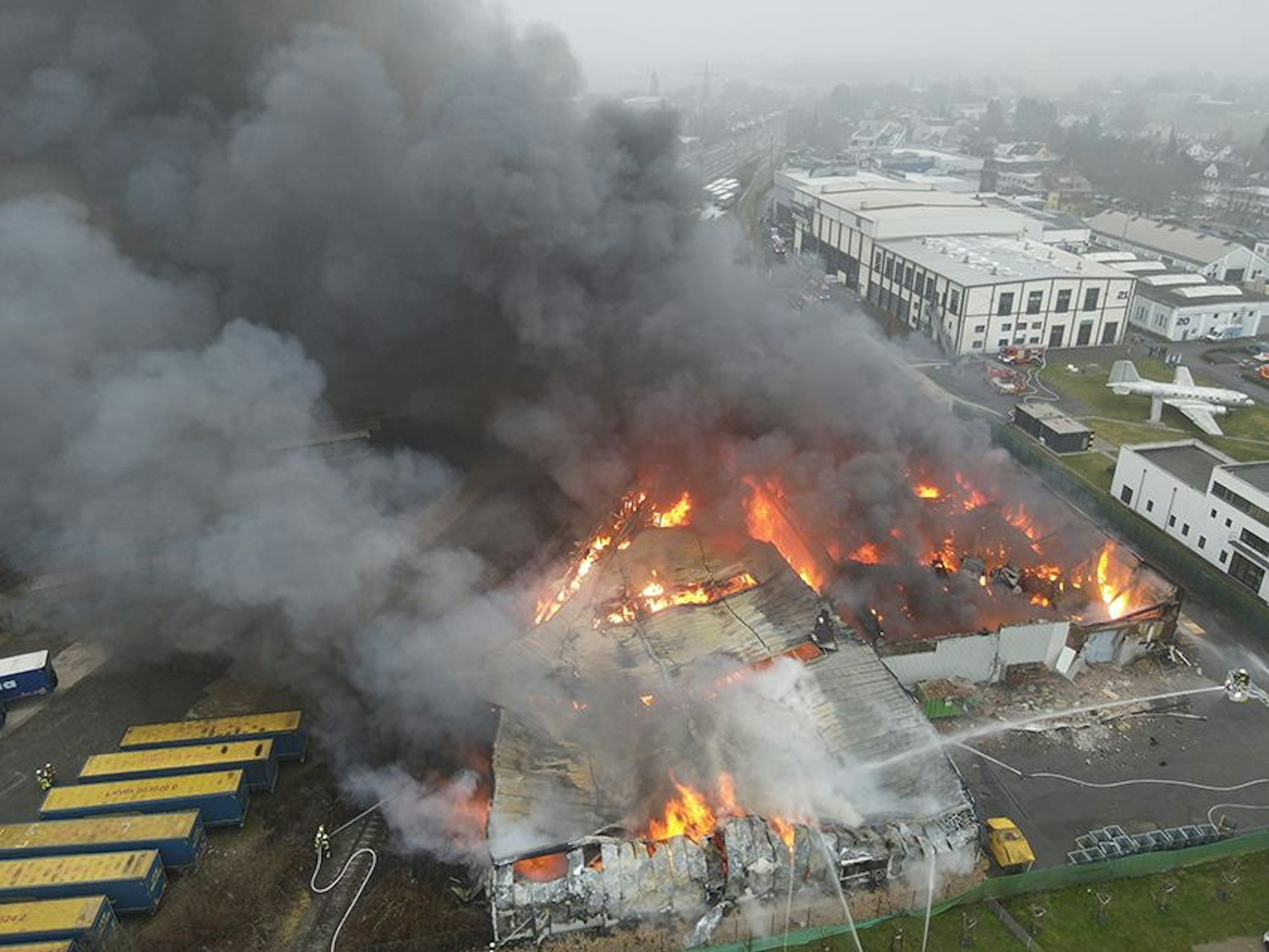 Das Bild ist einer Drohneaufnahme und zeigt zwei brennende Lagerhallen.