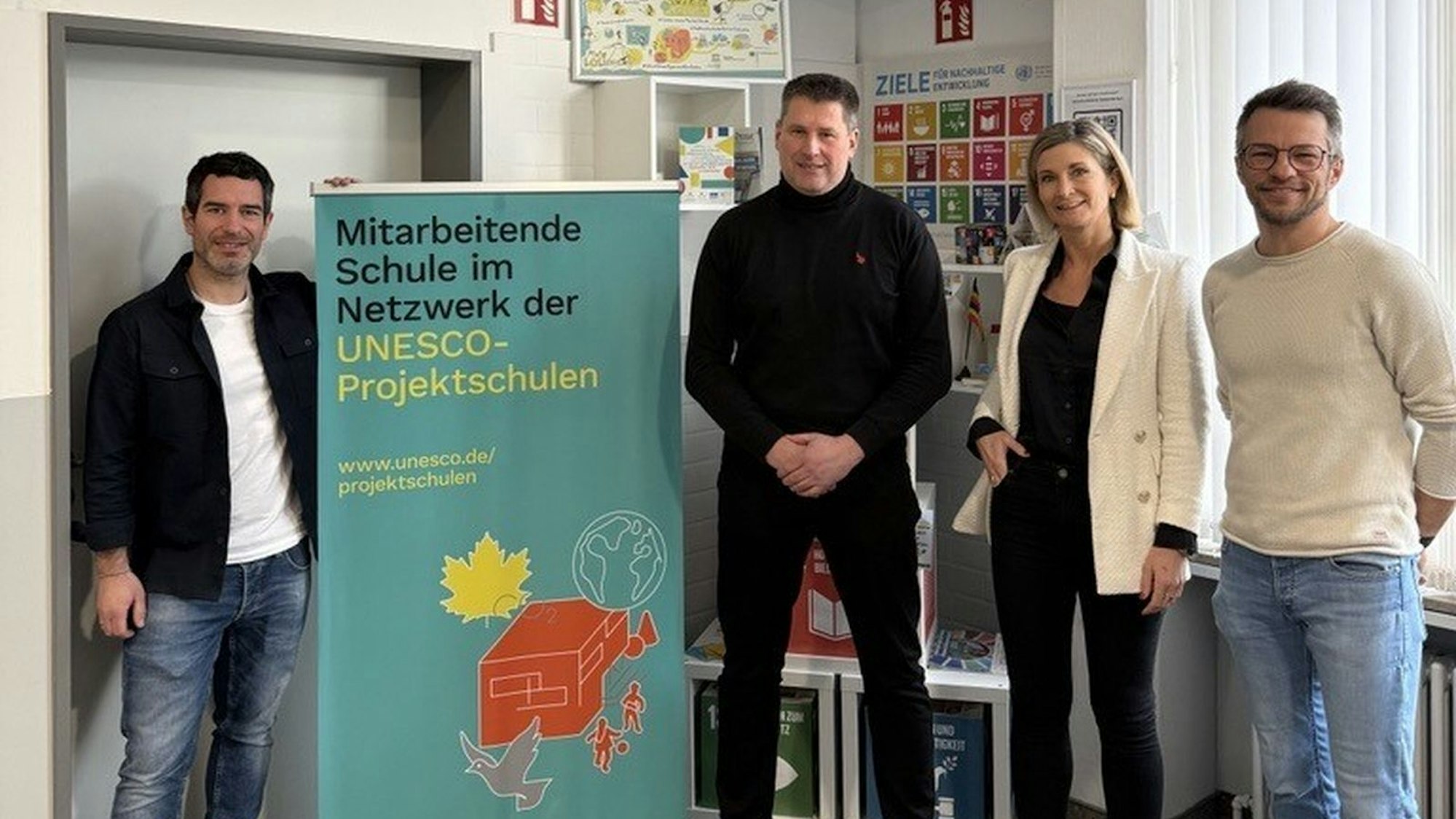 Drei Herren und eine Dame neben einer Stellwand.