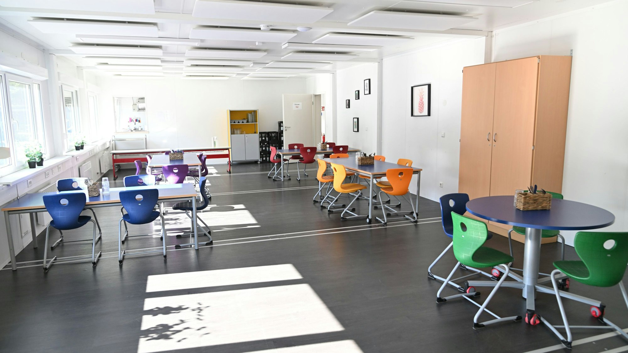 Innenraum eines hellen Unterrichtscontainers mit bunten Tischen und Stühlen.