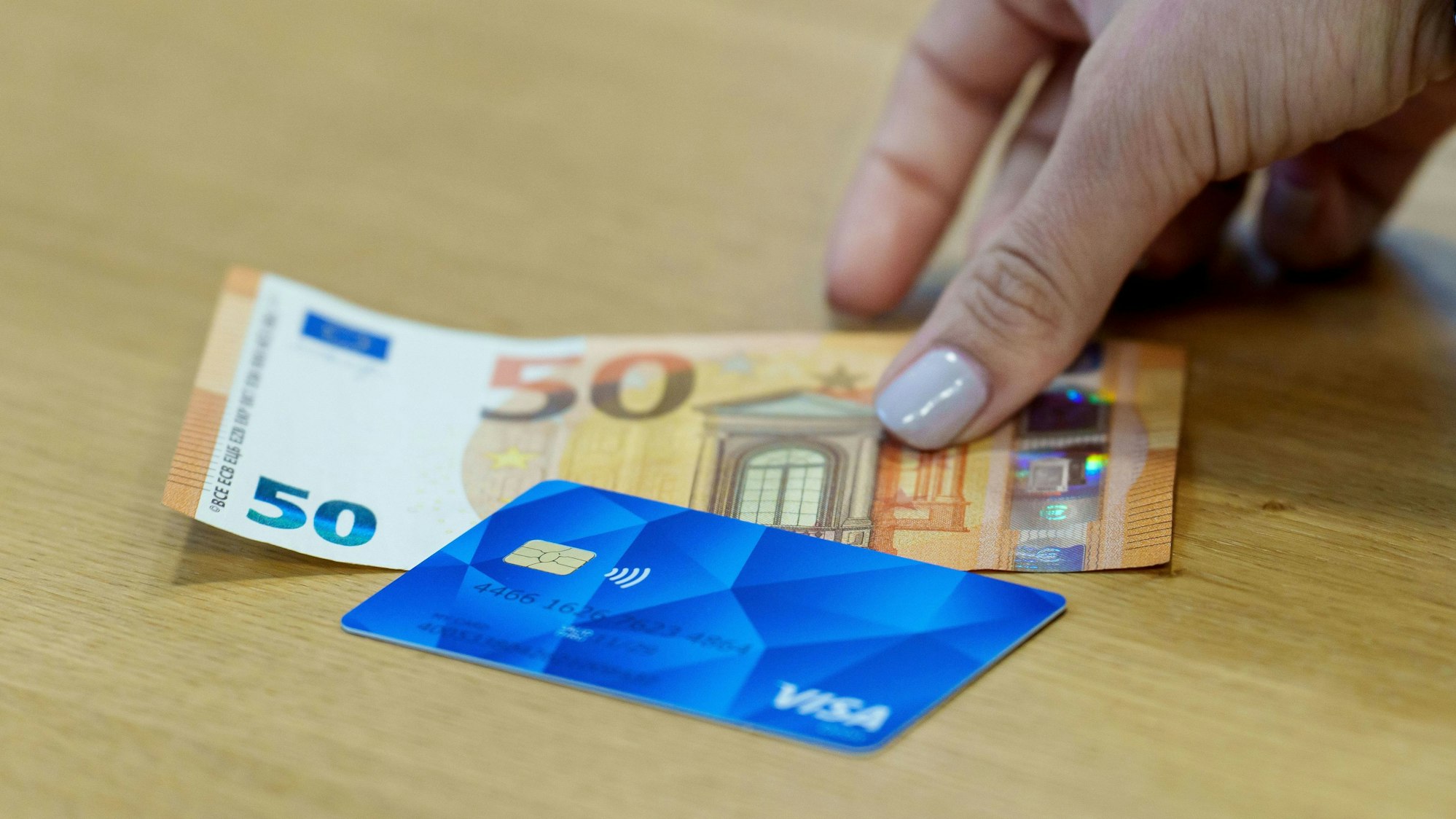 Eine Bezahlkarte für Asylbewerberinnen und Asylbewerber und ein 50 Euro Schein liegen nebeneinander.