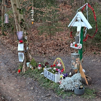 Neben einer Straße mit rot-weißen Warntafeln in einer Kurve steht ein Kreuz, das an einen tödlichen Unfall erinnert.