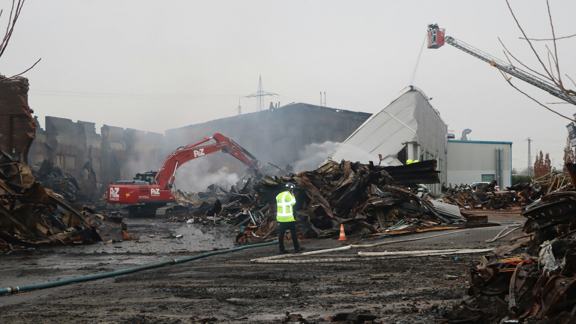 Noch war das Feuer am Mittwochmorgen nicht gänzlich gelöscht. Ein Bagger zieht Schutt auseinander, damit die Feuerwehrleute zu Glutnestern vordringen kann.