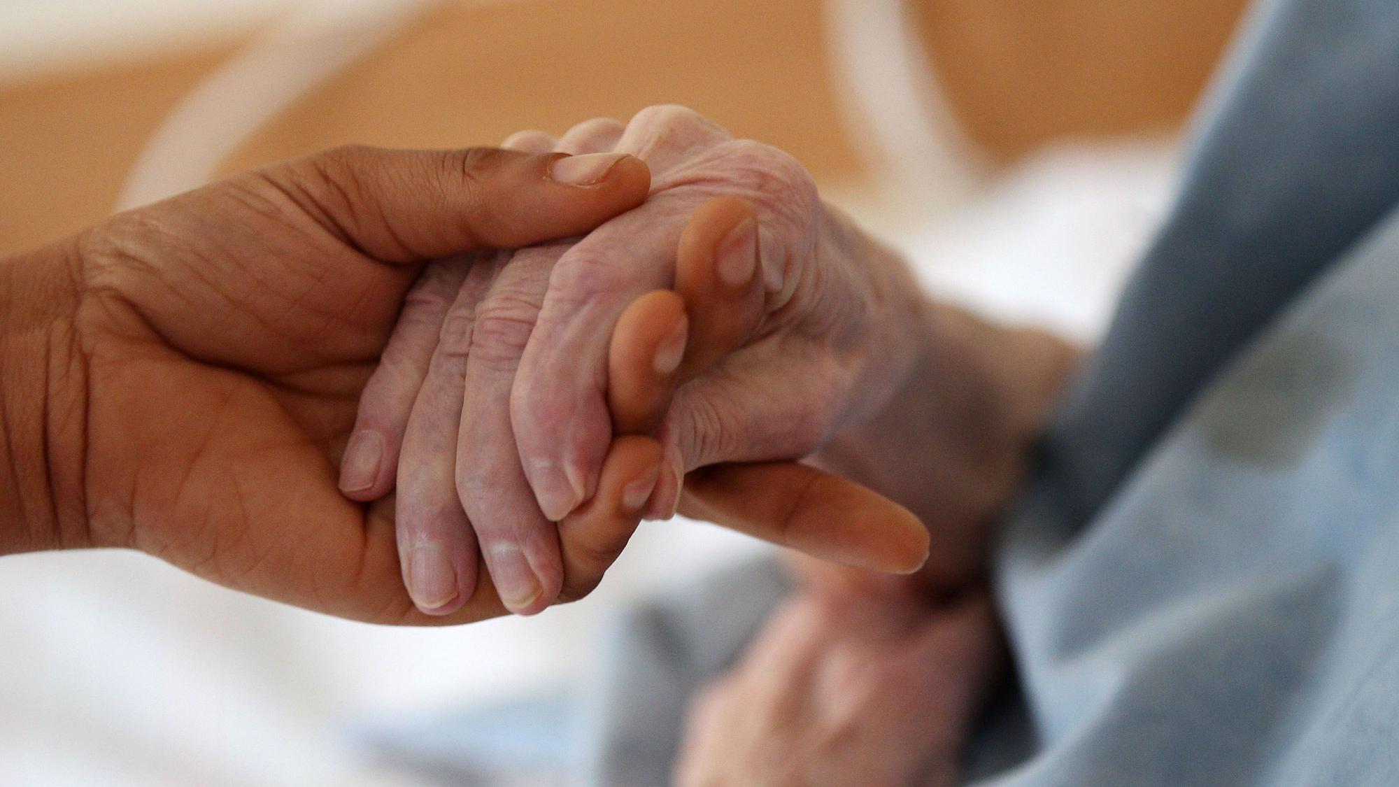 Das Bild zeigt eine junge Hand, die eine ältere hält.