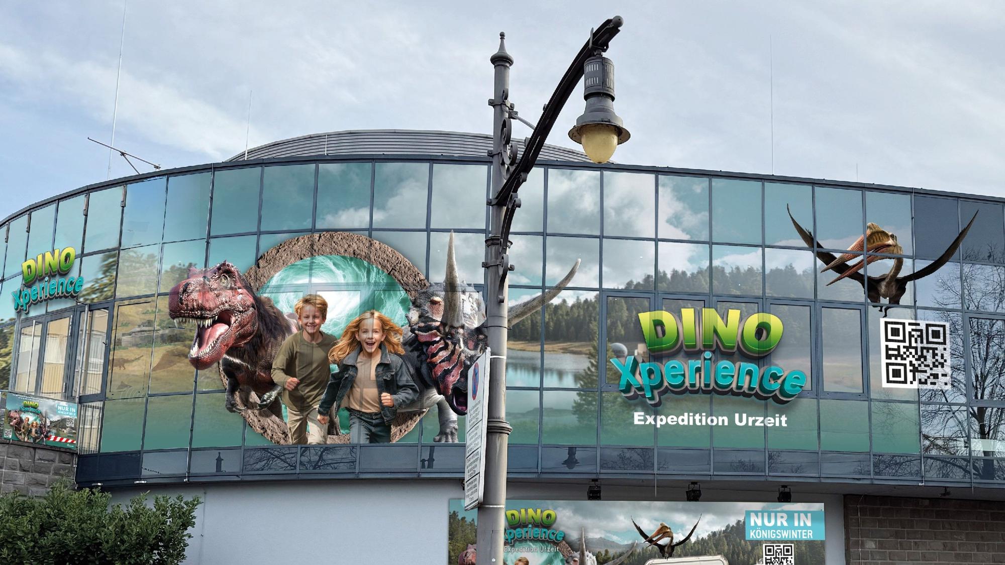 Große Darstellungen von Kindern und Dinosauriern an der Glasfassade eines Gebäudes.