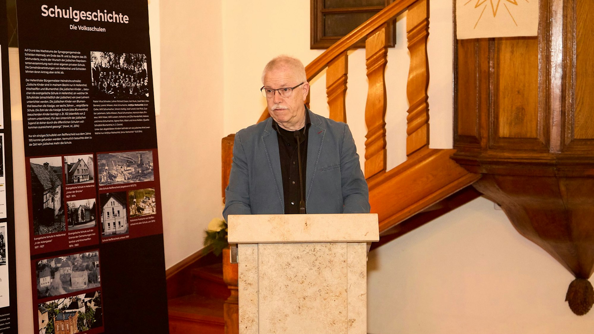 Das Bild zeigt den Obengenannten während der Rede. Er steht an einem Rednerpult.