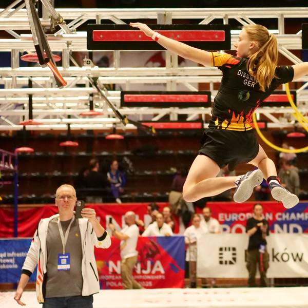 Szene aus dem Ninja-Sport, eine junge Frau hangelt durch einen Hindernisparcours.