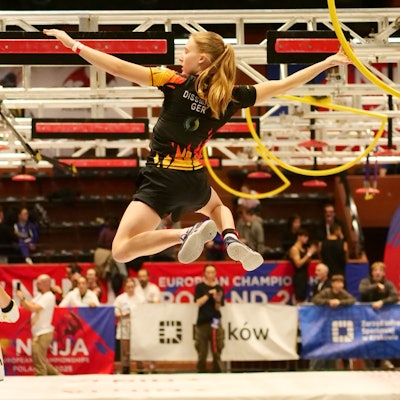 Szene aus dem Ninja-Sport, eine junge Frau hangelt durch einen Hindernisparcours.